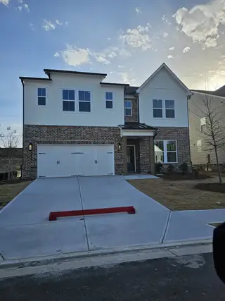 Street view A modern farmhouse with brick and white siding, featuring a charming covered porch in The Paddocks at Doc Hughes by Beazer Homes (Buford, GA).