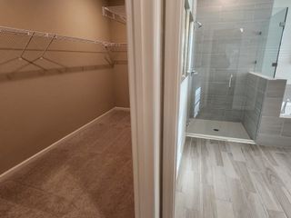 Model Home A spacious walk-in closet with ample shelving beside a sleek, modern shower with gray tiles and glass enclosure.