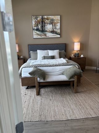 Model Home A cozy bedroom with modern bedding, textured rug, ambient lighting, and serene landscape artwork on the wall.