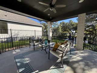 Model Home A serene backyard seating area with a fire pit, black chairs, lush greenery, and oak trees, creating a peaceful outdoor retreat.