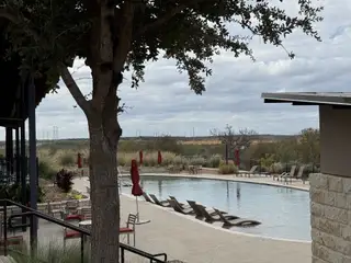 Community Amenities A serene poolside area with lounge chairs and umbrellas in Whisper Valley by Terrata Homes (Manor, TX).