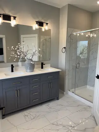 A modern bathroom featuring a sleek gray vanity, elegant lighting, and a spacious glass-enclosed marble shower.