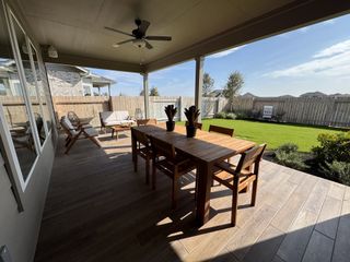 A charming covered patio with wooden furniture, ceiling fan, and a view of a private, fenced backyard.