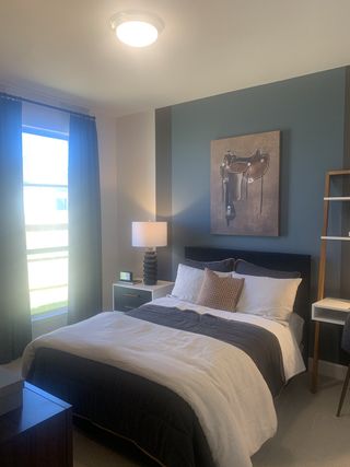 A cozy bedroom with a plush bed, modern artwork, stylish nightstand, and a warm-lit lamp.