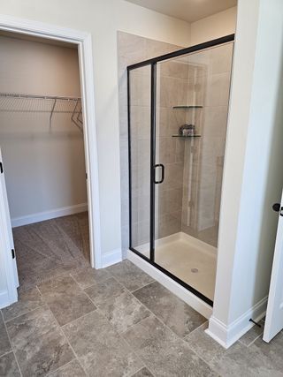 A modern bathroom featuring a sleek glass shower and walk-in closet, complemented by elegant stone tile flooring.