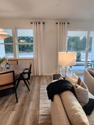 A cozy dining and living area with large windows, white curtains, and stylish furnishings.