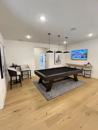 A sophisticated game room featuring a sleek black pool table, stylish pendant lights, and warm wooden floors.