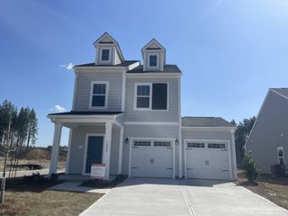 Street view A stylish modern farmhouse with gray siding, dormer windows, and a covered front porch in Homecoming by True Homes (Ravenel, SC).