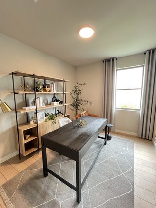 A modern office with a sleek desk, stylish shelving, and elegant decorations. Light floods in through a large window.