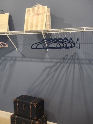 Model Home A neatly organized closet with a wire shelf, hangers, decorative bags, and vintage-style chests on a blue wall.