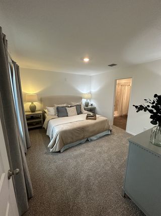A cozy bedroom with a soft carpet, elegant bedding, and soft lighting, leading to an adjoining bathroom.