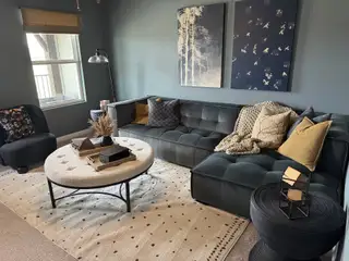 A cozy living room with a plush dark sofa, stylish artwork, and a round tufted coffee table on a chic patterned rug.