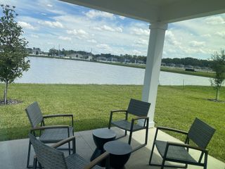 A serene patio with wicker chairs overlooking a calm lake and green lawn. Ideal for relaxation and outdoor gatherings.