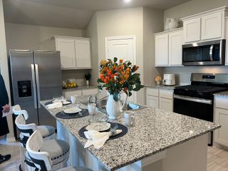 Modern kitchen with granite island, white cabinets, stainless steel appliances, and elegant barstools.