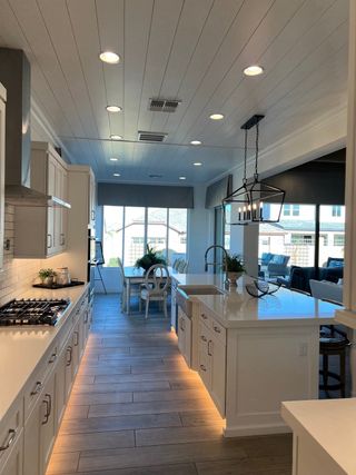A modern kitchen with sleek white cabinetry, under-cabinet lighting, and elegant fixtures leading to a bright dining area.
