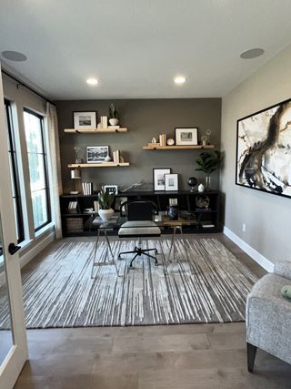 A modern home office featuring sleek shelving, abstract art, and a large window flooding the room with natural light.