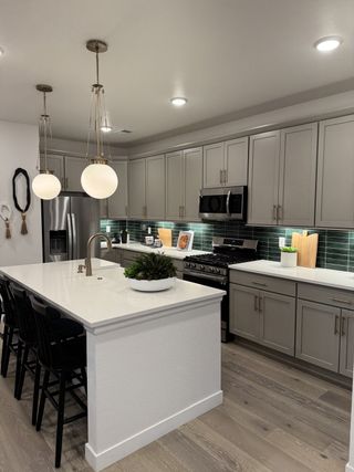 A modern kitchen with a sleek island, warm wood floors, gray cabinets, and pendant lighting over the countertop.