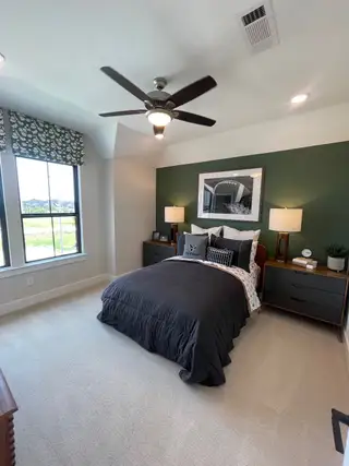 Model Home A cozy bedroom with a green accent wall, modern ceiling fan, and stylish black bedding, creating a sleek, relaxing vibe.