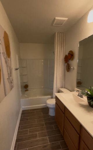 A functional bathroom in The Granary home, featuring a combination tub and shower, a modern vanity with dual sinks, and wood-look tile flooring (San Antonio, TX).