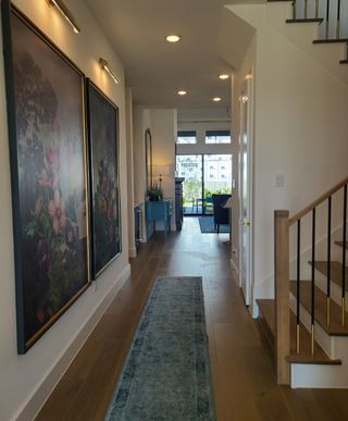 A bright hallway with floral paintings, a blue runner, and wooden flooring leading to a stylish living space.
