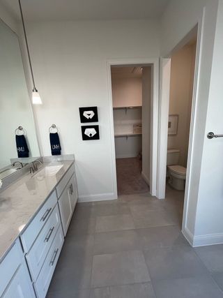 A modern bathroom with sleek white cabinetry, pendant lighting, and access to a spacious walk-in closet.