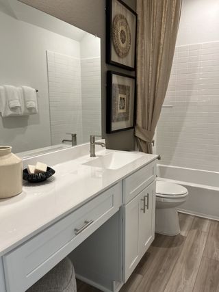 A modern bathroom with sleek white cabinetry, framed art, and stylish tile accents.