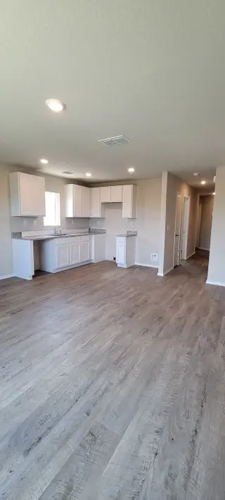 A modern kitchen with sleek white cabinets, granite countertops, and recessed lighting on hardwood floors.