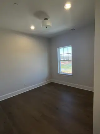 A bright bedroom with sleek wooden floors, soft gray walls, and a modern ceiling light fixture.