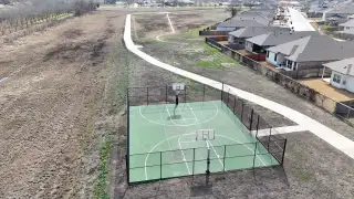 Community Amenities An aerial view of a community basketball court, surrounded by walking trails and nearby homes, offering great outdoor activity options for residents.