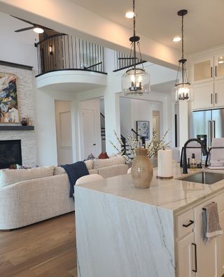 Model Home A modern living space with a marble island, elegant lighting, and a cozy seating area under a sweeping staircase.