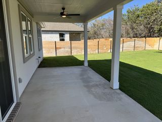 Model Home A spacious covered patio with a ceiling fan overlooks a lush green lawn and wooden fence for privacy.