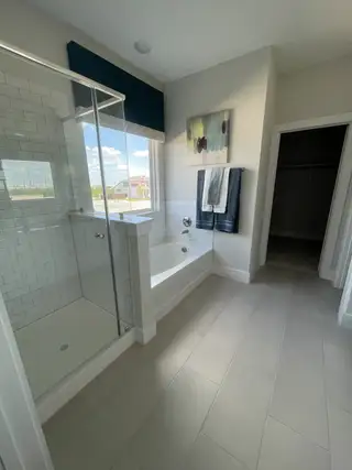 Model Home A modern bathroom with a glass shower, tiled floor, and sleek bathtub, offering a serene and stylish escape.