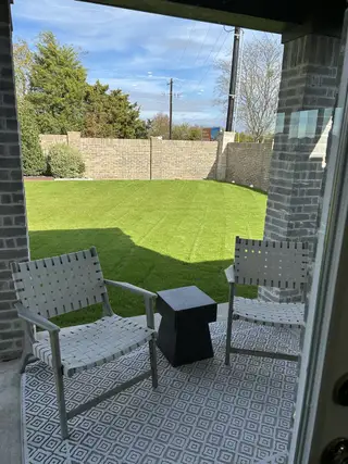 Model Home A cozy patio with two chairs, a geometric rug, and a small table overlooks a lush, fenced yard under blue skies.