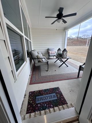 A cozy covered porch with seating, ceiling fan, and welcome mat, perfect for relaxing outdoors.