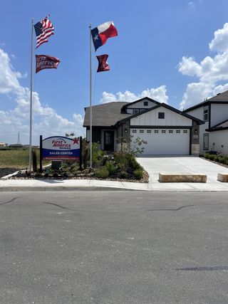 Charming home with flags, driveway, and landscaping in Red Hawk Landing by First America Homes (San Antonio, TX).