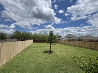 A spacious fenced backyard with lush greenery in McKinney Crossing by KB Home (Austin, TX).