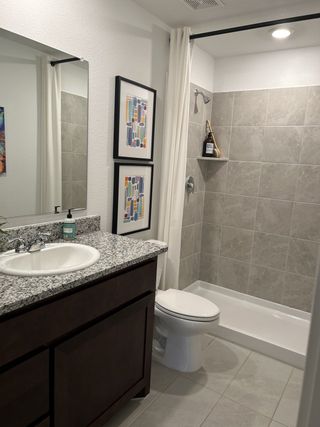 A functional bathroom with dark cabinetry, a granite countertop, and a tiled shower.
