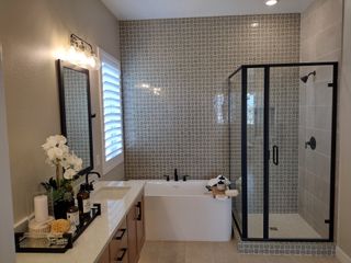 A modern bathroom featuring a grid-tiled shower, elegant bathtub, and sleek vanity with stylish lighting.