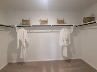 Model Home A spacious walk-in closet with cozy carpet, featuring baskets and plush white robes on elegant shelving.