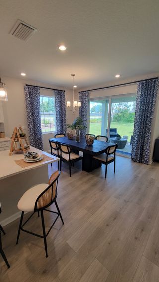 Model Home A cozy dining area with wood floors, elegant lighting, and sliding doors opening to a lush outdoor view.