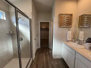 Model Home A modern bathroom featuring a glass walk-in shower, dual sinks, and chic artwork on the wall.