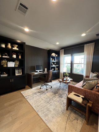 Model Home A cozy home office featuring a sleek desk, plush seating, modern shelves, and soft lighting, creating an inviting work atmosphere.