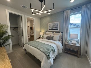 A cozy bedroom featuring a modern chandelier, soft bedding, and subtle decor with a serene atmosphere.