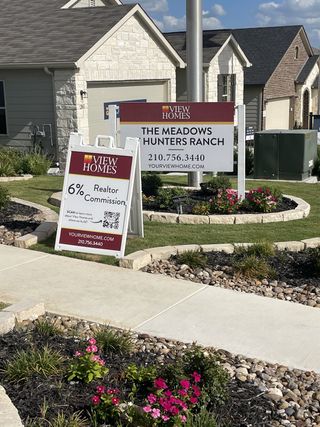 A well-manicured lawn with colorful flowers and a View Homes sign at The Meadows at Hunters Ranch (San Antonio, TX), showcasing a welcoming community entrance. 