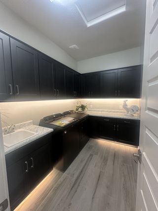 A sleek laundry room with black cabinetry, marble countertops, recessed lighting, and a modern utility sink.
