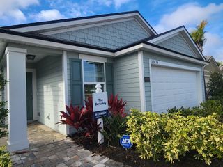 A coastal-inspired home with blue shutters, lush landscaping, and a cozy porch at The Arbors by D.R. Horton (Jacksonville, FL).