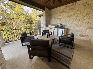 A cozy outdoor patio with a stone wall, comfy seating, and a built-in grill under a wooden ceiling. Ideal for relaxation.