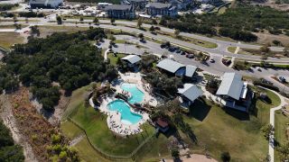 Community Amenities A breathtaking aerial view of the Headwaters community, showcasing an infinity-edge pool, scenic trails, and lush green spaces in Headwaters by David Weekley Homes (Dripping Springs, TX).