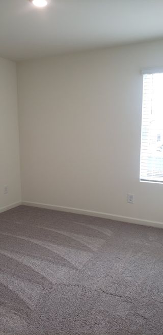 A bright room with soft carpet, light walls, and natural light filtering through a window with blinds.
