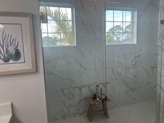 A sleek bathroom featuring marble-patterned tiles, a glass shower, and a coastal-themed artwork for a serene ambiance.